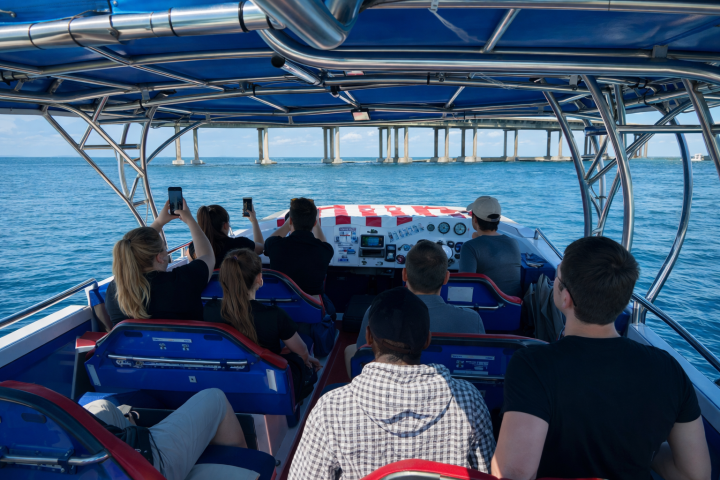 People on a boat under a bridge, taking photos of the scenery over a blue ocean.