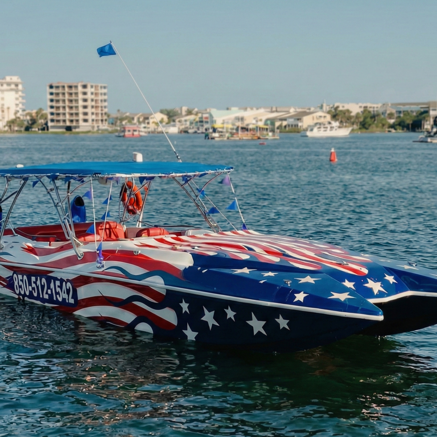 Boat with US flag design on water, city buildings in background.