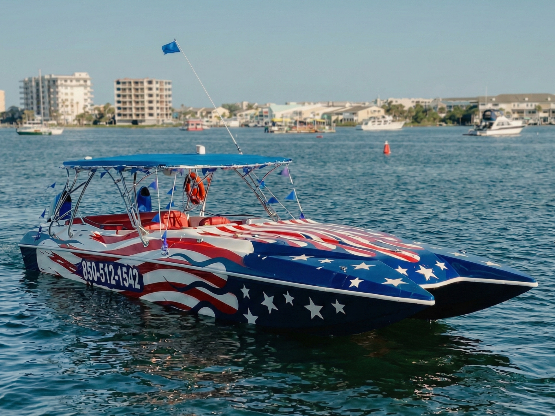 Boat with US flag design on water, city buildings in background.