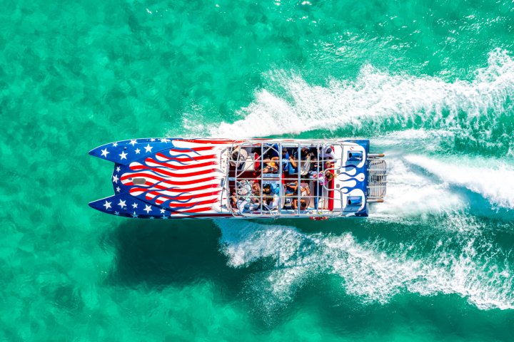 Aerial view of boat with American flag design speeding on turquoise water.