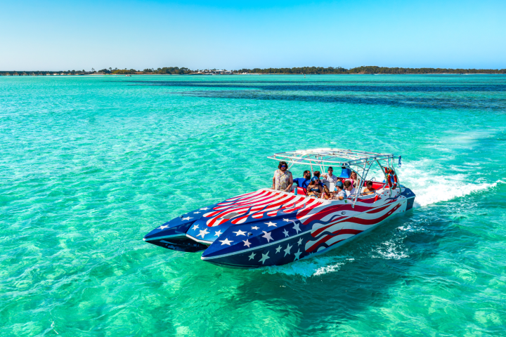 Speedboat with American flag design on turquoise water under a clear blue sky.