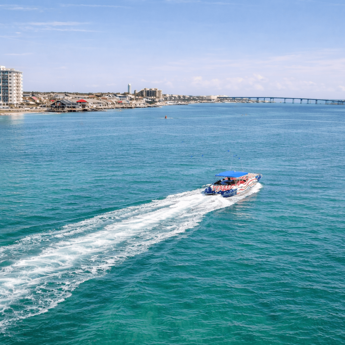 Speedboat on blue water near coastal city with bridge and buildings in background.