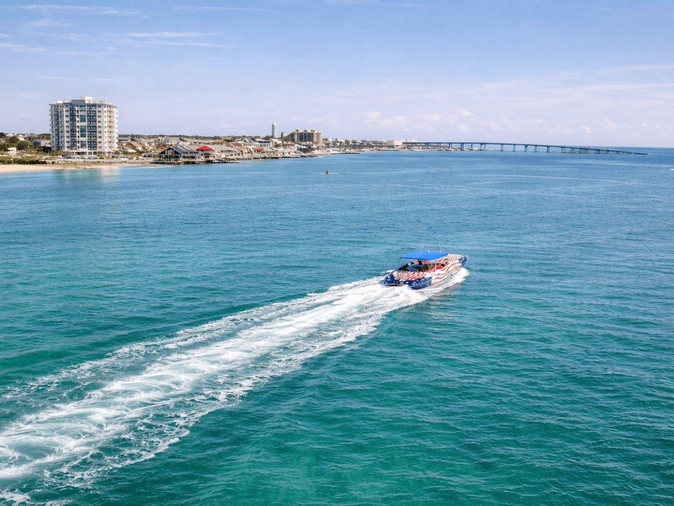 Speedboat on blue water near coastal city with bridge and buildings in background.