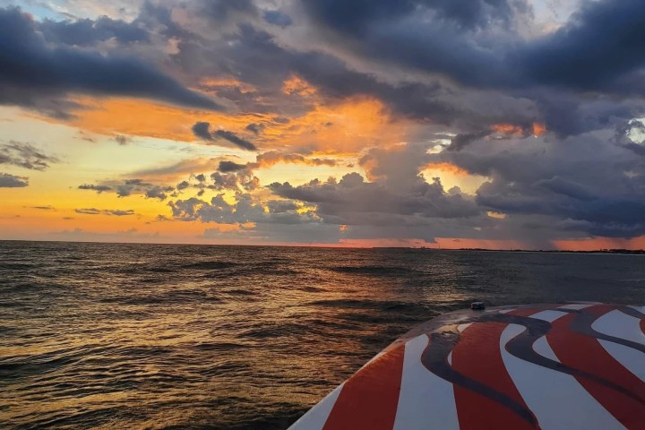 Sunset over ocean with colorful clouds and boat bow in the foreground.