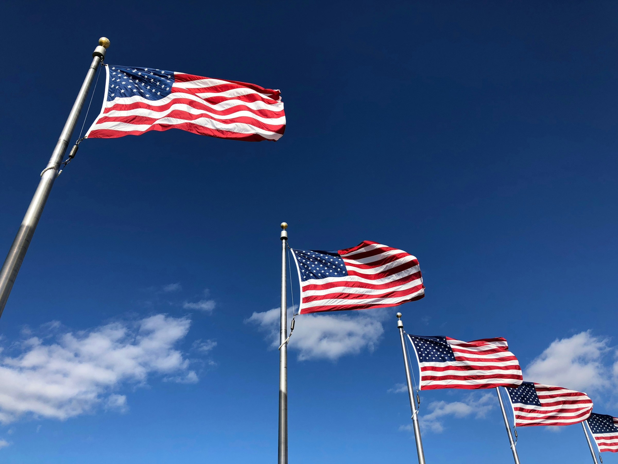 Four American flags waving against a clear blue sky.