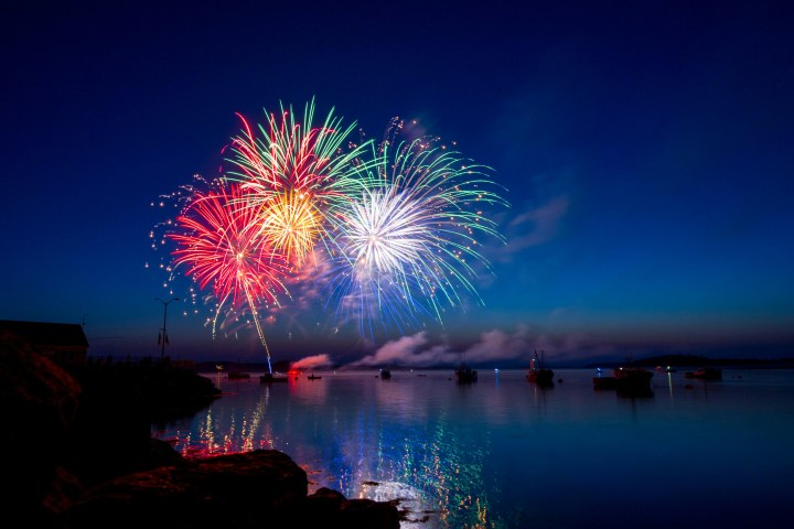 Colorful fireworks over water with boats at dusk.